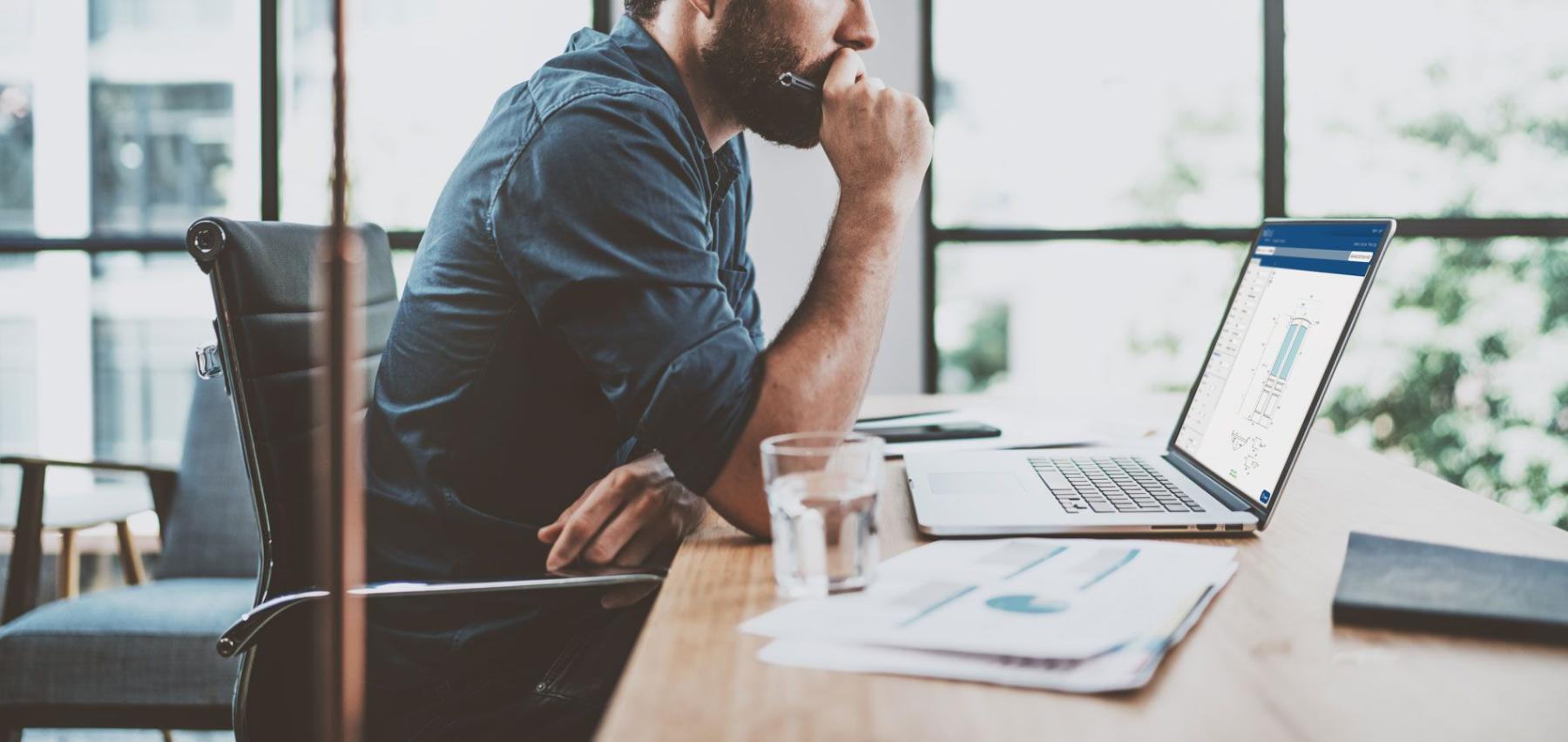 bearded man at office desk looking at a laptop looking at custom door designer online