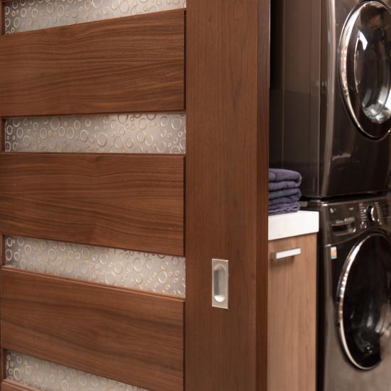 A TM9350 barn door in walnut with Nutmeg stain and Bamboo Rings resin conceals the laundry room from the dining room.