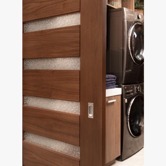 A TM9350 barn door in walnut with Nutmeg stain and Bamboo Rings resin conceals the laundry room from the dining room.